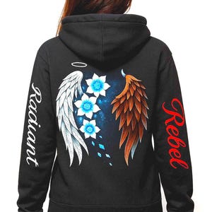 May include: Black hoodie with a design featuring angel wings, blue flowers, and the words "Radiant" and "Rebel." The wings are white and brown, and the flowers have blue centers. The text is in white and red.