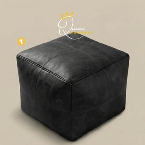 May include: A square, black leather ottoman with stitched detailing. The ottoman is a cube shape and appears to be made of a distressed leather material. The text "Queen Handmade" is in the upper right corner.