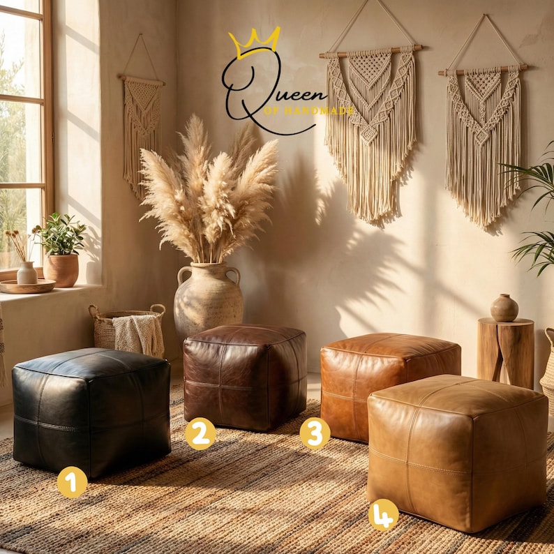 May include: Four leather ottomans in black, dark brown, medium brown, and light brown are arranged on a woven rug. The ottomans are square and have stitched details. The background includes decorative wall hangings, a large vase with pampas grass, and a window.