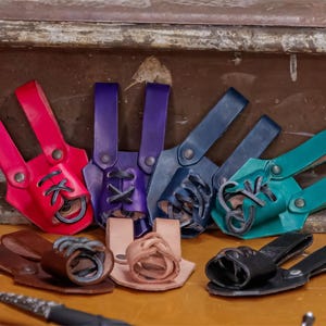 May include: A set of eight leather loops in various colors, including red, blue, green, and brown. The loops are designed to hold small items, such as keys or tools.
