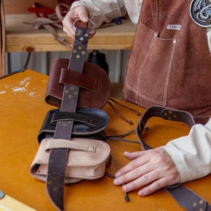 Puede incluir: Un conjunto de cuatro bolsas de cuero marr&oacute;n con hebillas y correas de metal. Las bolsas est&aacute;n unidas a un cintur&oacute;n de cuero marr&oacute;n con una hebilla de metal. Las bolsas cuelgan de una mesa de madera.
