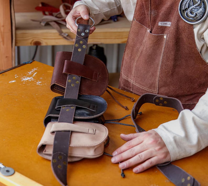 Puede incluir: Un conjunto de cuatro bolsas de cuero marr&oacute;n con hebillas y correas de metal. Las bolsas est&aacute;n unidas a un cintur&oacute;n de cuero marr&oacute;n con una hebilla de metal. Las bolsas cuelgan de una mesa de madera.
