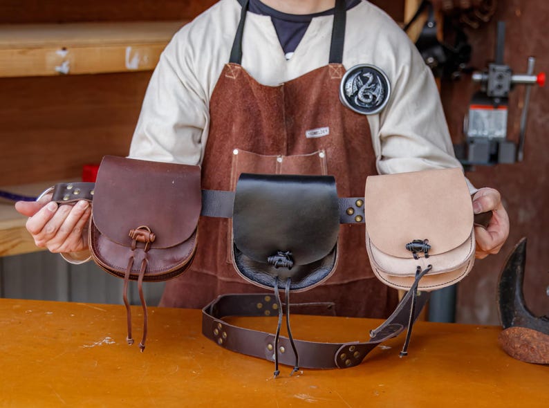 Puede incluir: Tres bolsas de cuero con hebillas y correas, usadas en un cintur&oacute;n de cuero marr&oacute;n. Las bolsas son marr&oacute;n, negro y beige.