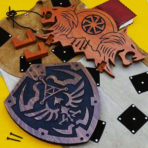 May include: Wooden decorative items, including a shield with a crest, a wolf-like figure, and small wooden blocks. The shield is dark blue with a brown border and a detailed emblem. The wolf figure is brown with intricate cutouts.