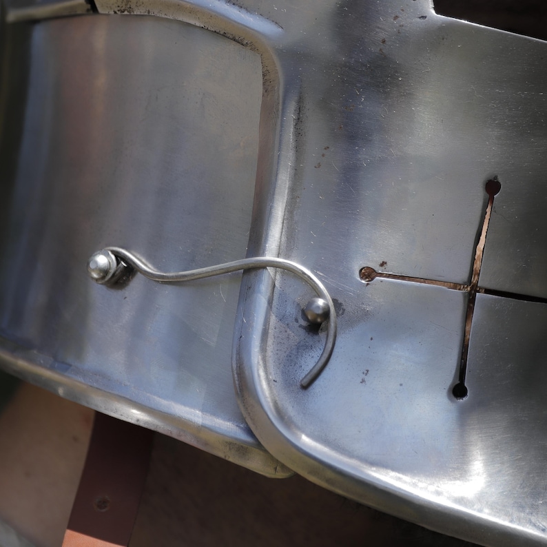 Pu&ograve; includere: Una piastra in metallo color argento lucido dotata di un meccanismo di chiusura a filo curvo fissato da due rivetti arrotondati. La superficie metallica presenta un ritaglio a forma di croce con estremit&agrave; circolari che riflette la luce.