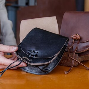Puede incluir: Tres bolsas de cuero con correas y hebillas de diferentes colores. Las bolsas son de cuero marr&oacute;n, negro y beige.