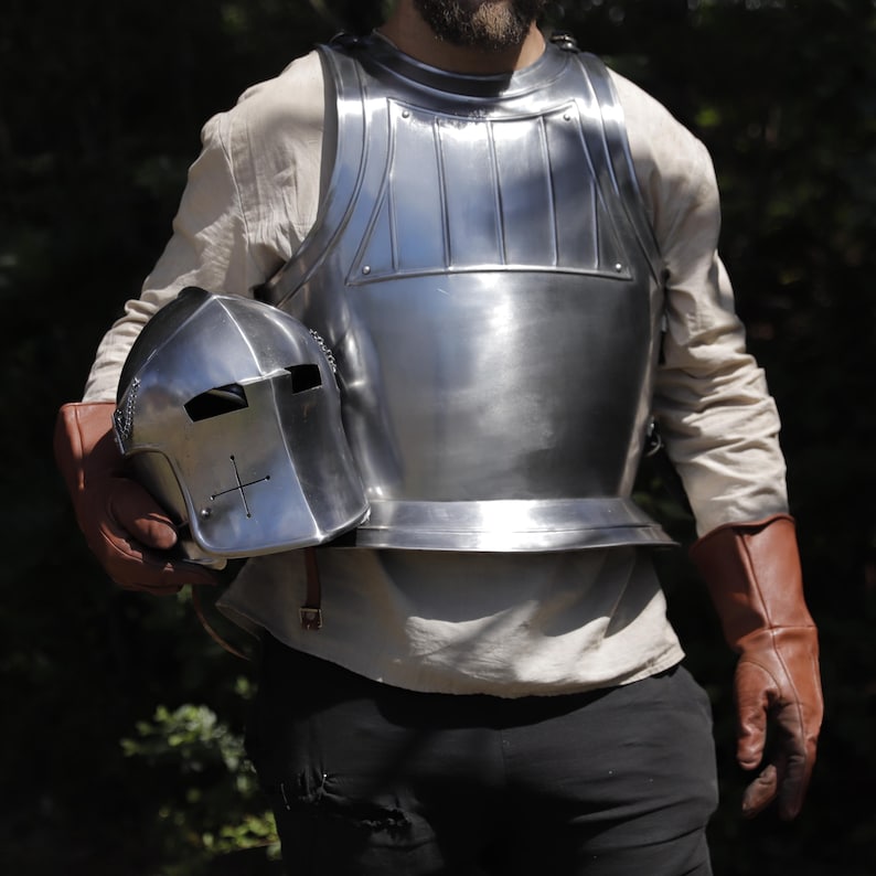 Pu&ograve; includere: Una corazza in acciaio lucido con nervature verticali sul petto superiore e un elmo in acciaio abbinato con un'apertura di ventilazione a forma di croce. L'armatura &egrave; indossata sopra una camicia a maniche lunghe con guanti in pelle marrone.