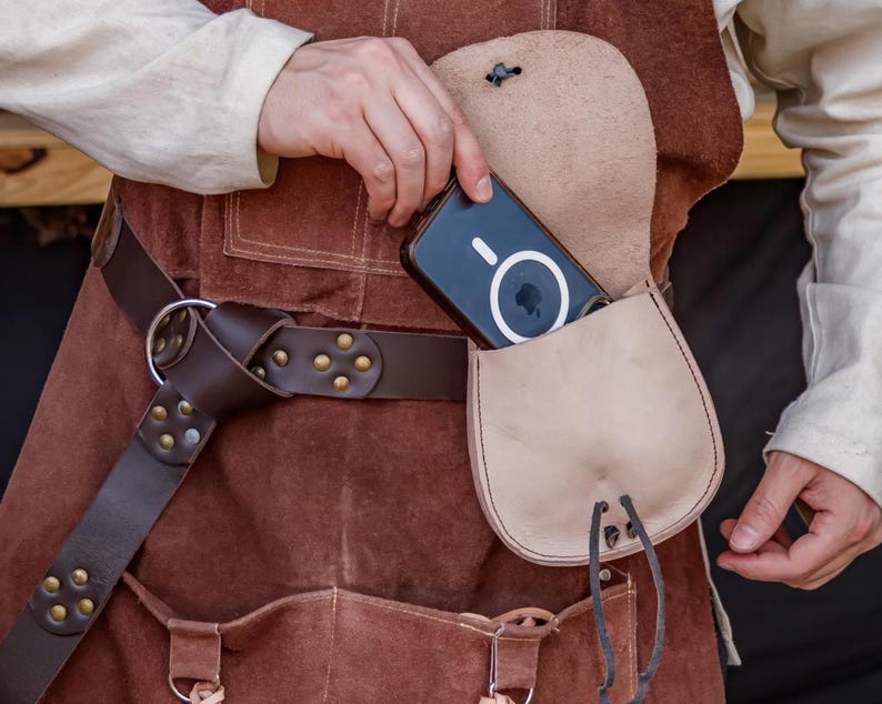 Puede incluir: Un cintur&oacute;n de cuero marr&oacute;n con una hebilla plateada y una bolsa de cuero marr&oacute;n con un tel&eacute;fono negro en su interior. La bolsa est&aacute; unida al cintur&oacute;n con una correa de cuero marr&oacute;n.