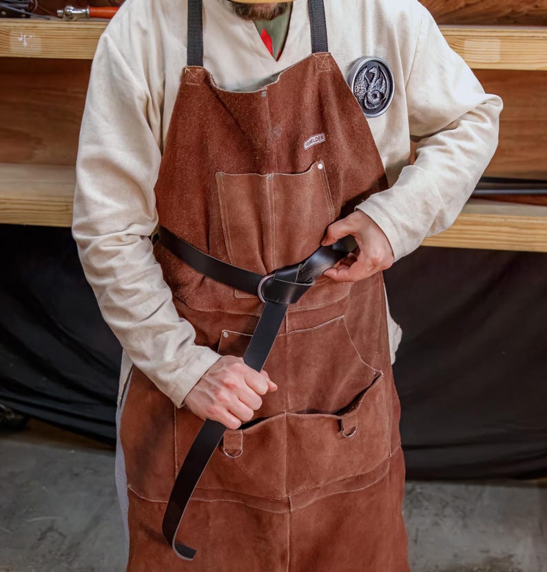 May include: A person wearing a brown leather apron with a black leather belt. The belt has a metal buckle and is tied in a knot.