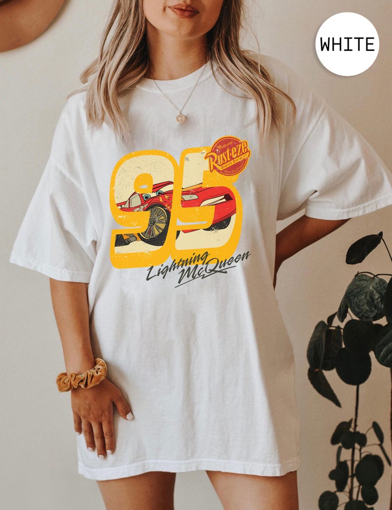 May include: White t-shirt featuring a graphic of Lightning McQueen from the movie Cars. The design includes the number 95 in yellow, a red race car, and the text "Lightning McQueen" in black.