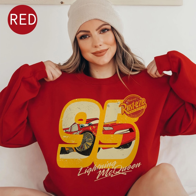 May include: Red sweatshirt featuring a graphic of Lightning McQueen from the movie Cars. The design includes the number 95, the Rust-eze logo, and the text "Lightning McQueen". The sweatshirt is a solid red color.