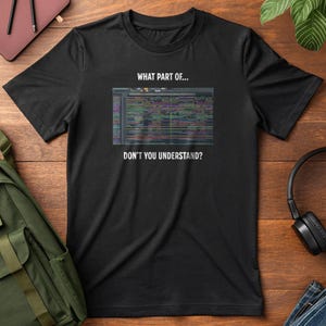 Może przedstawiać: Czarny t-shirt z napisem "WHAT PART OF... DON'T YOU UNDERSTAND?" nad i pod kolorową grafiką. Grafika wydaje się być zrzutem ekranu interfejsu cyfrowej stacji roboczej audio. Koszulka jest prezentowana na drewnianej powierzchni.