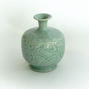 May include: A light blue ceramic vase with a floral design. The vase has a round body and a narrow neck.