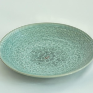 May include: A light green ceramic plate with a raised floral design. The plate has a delicate, intricate pattern and a subtle sheen.