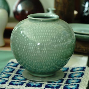 May include: A light green ceramic vase with a white geometric pattern. The vase has a round body and a wide opening.