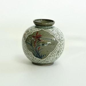 May include: A small, round, green ceramic vase with white floral designs and a red and blue floral painting.