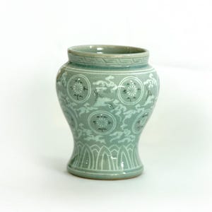 May include: A light green ceramic vase with a white and black design of stylized clouds and flowers. The vase has a rounded body and a flared base.