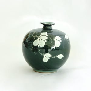 May include: A dark green ceramic vase with white floral designs. The vase has a round body and a narrow neck.