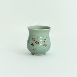 May include: A light blue ceramic teacup with a floral design. The cup has a rounded bottom and a wide mouth.