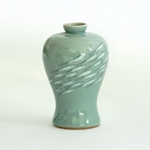 May include: A light blue ceramic vase with a design of white fish swimming in a school. The vase has a rounded body and a narrow neck.