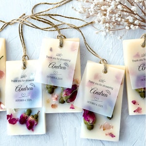 May include: Rectangular cream-colored wax bars embedded with dried pink rosebuds and petals. Each bar features a translucent vellum tag tied with twine, printed with the text Thank you for showering, the name Andrea, and OCTOBER 4, 2025.