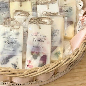 May include: Rectangular wax melts encased in clear plastic sleeves with twine loops. Each features a semi-transparent tag printed with 'Thank you for showering', the name 'Andrea', and 'OCTOBER 4, 2025'. Dried flower petals are embedded in the wax.