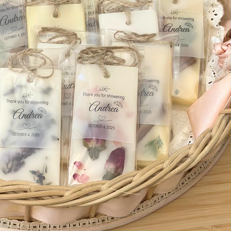 May include: Rectangular wax melts encased in clear plastic sleeves with twine loops. Each features a semi-transparent tag printed with 'Thank you for showering', the name 'Andrea', and 'OCTOBER 4, 2025'. Dried flower petals are embedded in the wax.