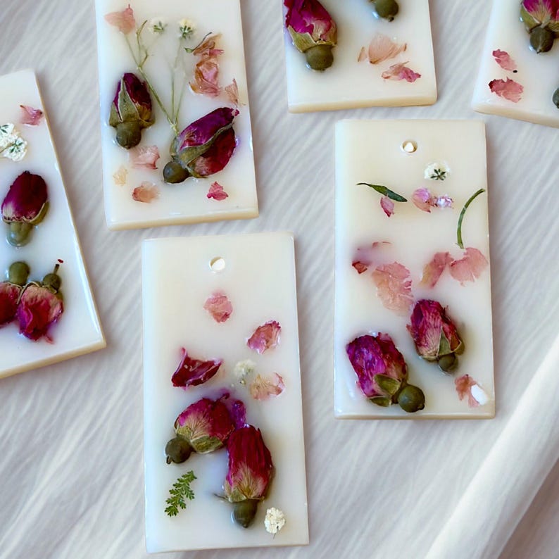 May include: Rectangular white wax tablets embedded with dried pink rosebuds, small green stems, and scattered flower petals. Each tablet features a small circular hole near the top edge, allowing for hanging or decorative display purposes.