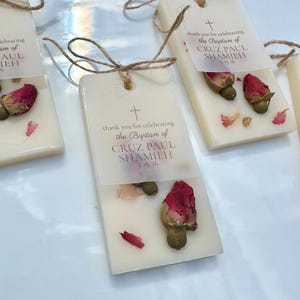 May include: Rectangular off-white wax bars decorated with dried red rosebuds and petals. Each bar features a translucent paper tag tied with twine, printed with a cross and the text: thank you for celebrating the Baptism of CRUZ PAUL SHAMIEH 3.15.26.