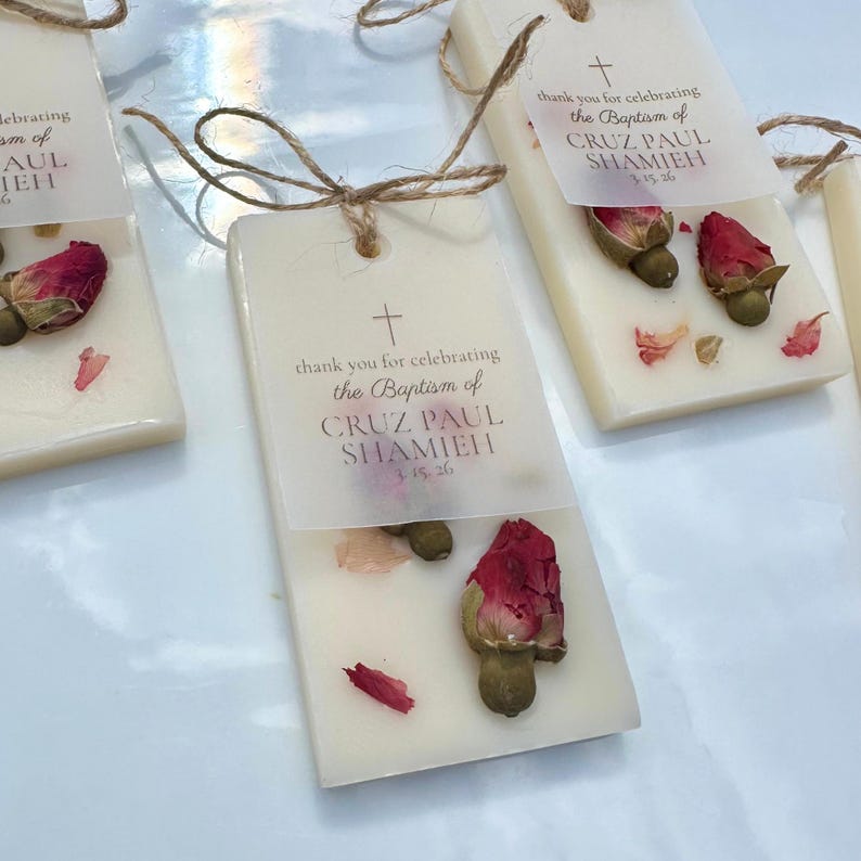 May include: Rectangular off-white wax bars decorated with dried red rosebuds and petals. Each bar features a translucent paper tag tied with twine, printed with a cross and the text: thank you for celebrating the Baptism of CRUZ PAUL SHAMIEH 3.15.26.