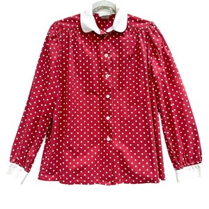 May include: A red long-sleeved blouse with white polka dots and a white Peter Pan collar. The blouse has white cuffs and a button-down front. The blouse is hanging on a white hanger.