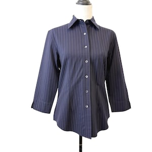 May include: A navy blue button-down shirt with vertical pinstripes. The shirt has three-quarter sleeves and a classic collar. The shirt is displayed on a mannequin.