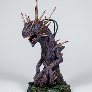 May include: A detailed, hand-painted fantasy creature figurine. The figure is primarily purple with brown and red accents, featuring sharp spikes and a menacing open mouth. It stands on a base with green foliage, showcasing intricate detailing.