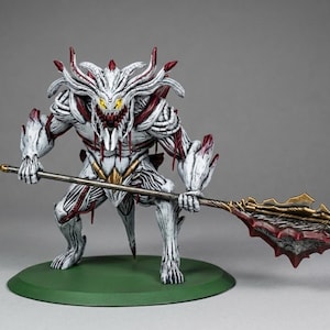 May include: A detailed figurine of a creature with a white and red colour scheme, holding a staff. The figure has a menacing expression with yellow eyes and sharp teeth. It stands on a green circular base.