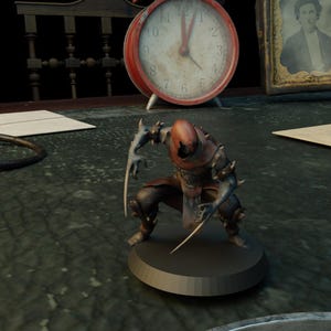 May include: A detailed figurine of a creature with a brown hooded head, dark armor, and sharp claws. The figure is kneeling on a round base. A red alarm clock and a framed portrait are in the background.