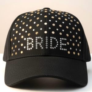 Peut inclure: Casquette de baseball noire avec le mot "BRIDE" en strass blancs. La casquette est ornée de strass dorés et argentés. La visière est noire et incurvée.