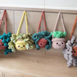 May include: Five crocheted plant pot purses hanging on a wall. Each purse has a different colored pot and plant, and a cute face with eyes and a smile. The purses are made with soft, colorful yarn.