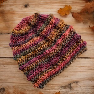May include: A crocheted beanie hat in shades of brown, orange, pink, and purple. The hat has a textured, bumpy surface.