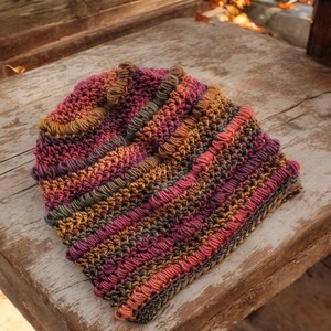 May include: A crocheted hat with a multi-colored striped pattern in shades of brown, orange, pink, and purple.
