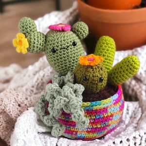 Pode incluir: Uma planta de cacto de crochê em um vaso colorido. O cacto é verde com flores amarelas e rosa. O vaso é um arco-íris de cores.