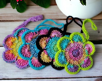 May include: Five crocheted flower-shaped ornaments with colorful yarn. Each ornament has a loop for hanging. The ornaments are in shades of purple, blue, green, yellow, and pink.