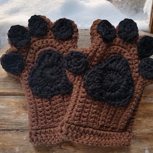 May include: A pair of brown crocheted paw print mittens with black crocheted paw pads.