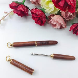 May include: Two wooden tools with a keychain loop. The larger tool has a metal tip and the text "NINI" engraved on the side. The smaller tool has a metal tip and a wooden handle.