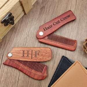 May include: Two wooden folding combs with engraved text. One comb reads "Hair Cut Crew" and the other has the initials "H|I|F". The combs are a reddish-brown color and are open and closed, showing the teeth.