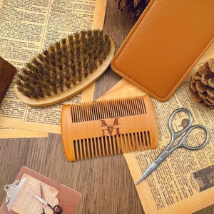 May include: A wooden comb with the engraved text "Mike" and a beard brush are displayed with a leather case and small scissors. The items are arranged on a wooden surface with vintage paper.