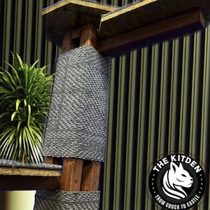 May include: A gray cat tree with a wooden base and two platforms. The platforms are covered in gray carpet. The cat tree is in front of a striped wall. The logo "The Kitten from Couch to Castle" is visible in the lower right corner of the image.