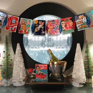 Pu&ograve; includere: Una ghirlanda di biglietti di Natale retr&ograve; con una variet&agrave; di motivi festivi, tra cui Babbo Natale, un razzo e un albero di Natale. La ghirlanda &egrave; appesa a una finestra con una scena innevata all'esterno. Ci sono due piccoli alberi di Natale artificiali sul tavolo sotto la finestra, insieme a una bottiglia di vino in una ghiacciaia e uno shaker per cocktail.