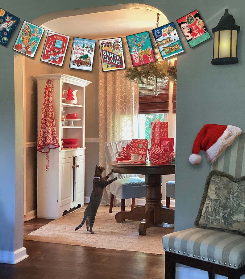 Pu&ograve; includere: Una ghirlanda natalizia con carte in stile vintage che mostrano immagini di Babbo Natale, renne e un albero di Natale. La ghirlanda &egrave; appesa in una stanza con un gatto, un tavolo e una sedia.
