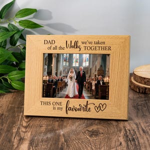 Puede incluir: Un marco de fotos de madera clara con una foto de boda. El marco tiene el texto "DAD of all the Walks we've taken TOGETHER THIS ONE is my favourite" con dos corazones. La foto muestra a una novia y su padre caminando por el pasillo.