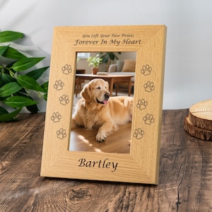 Puede incluir: Un marco de fotos de madera clara con una foto de un golden retriever. El marco tiene huellas de patas grabadas y el texto "You Left Your Paw Prints Forever In My Heart" y el nombre del perro "Bartley".